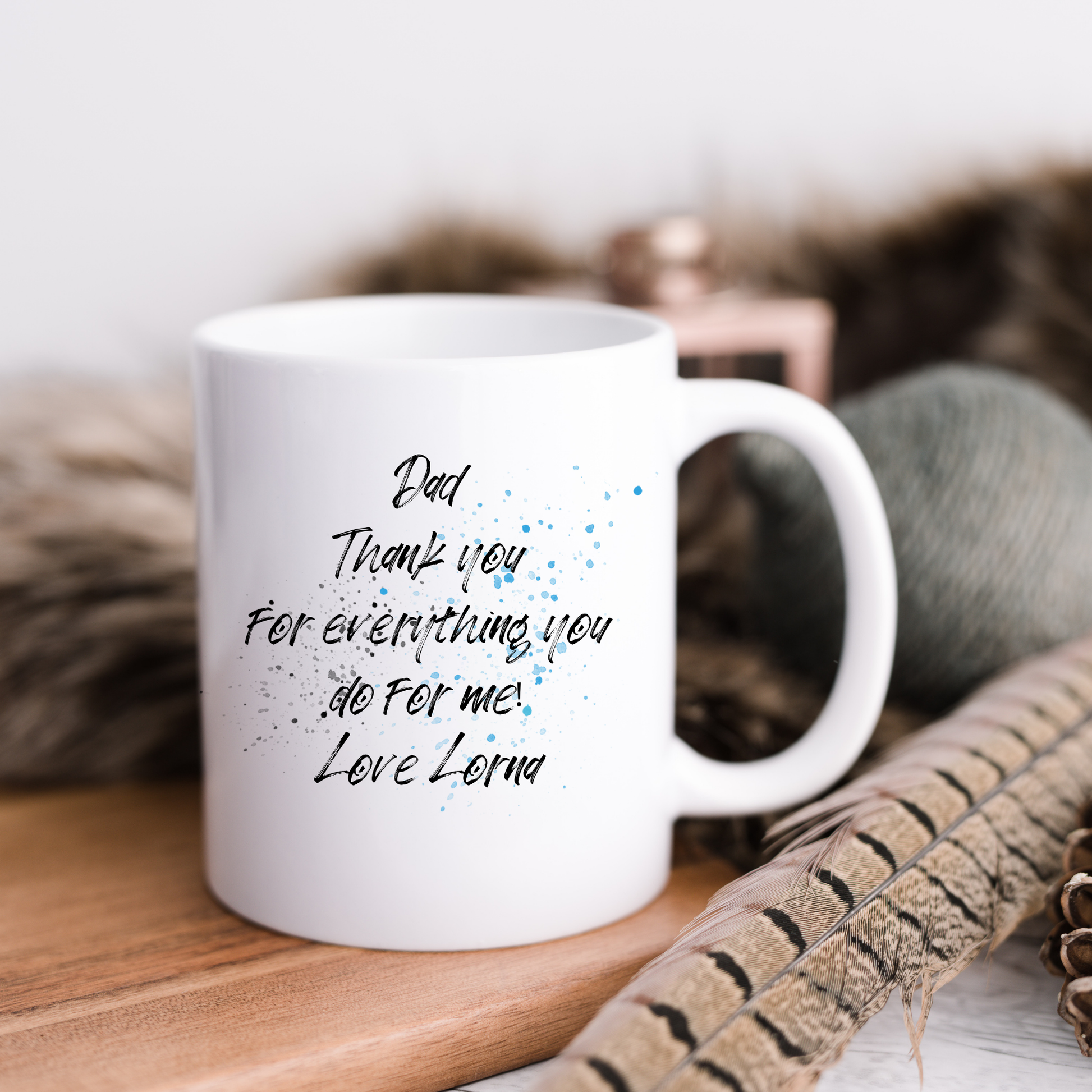 White mug with heartfelt message on a wooden surface with feathers and fabric in the background